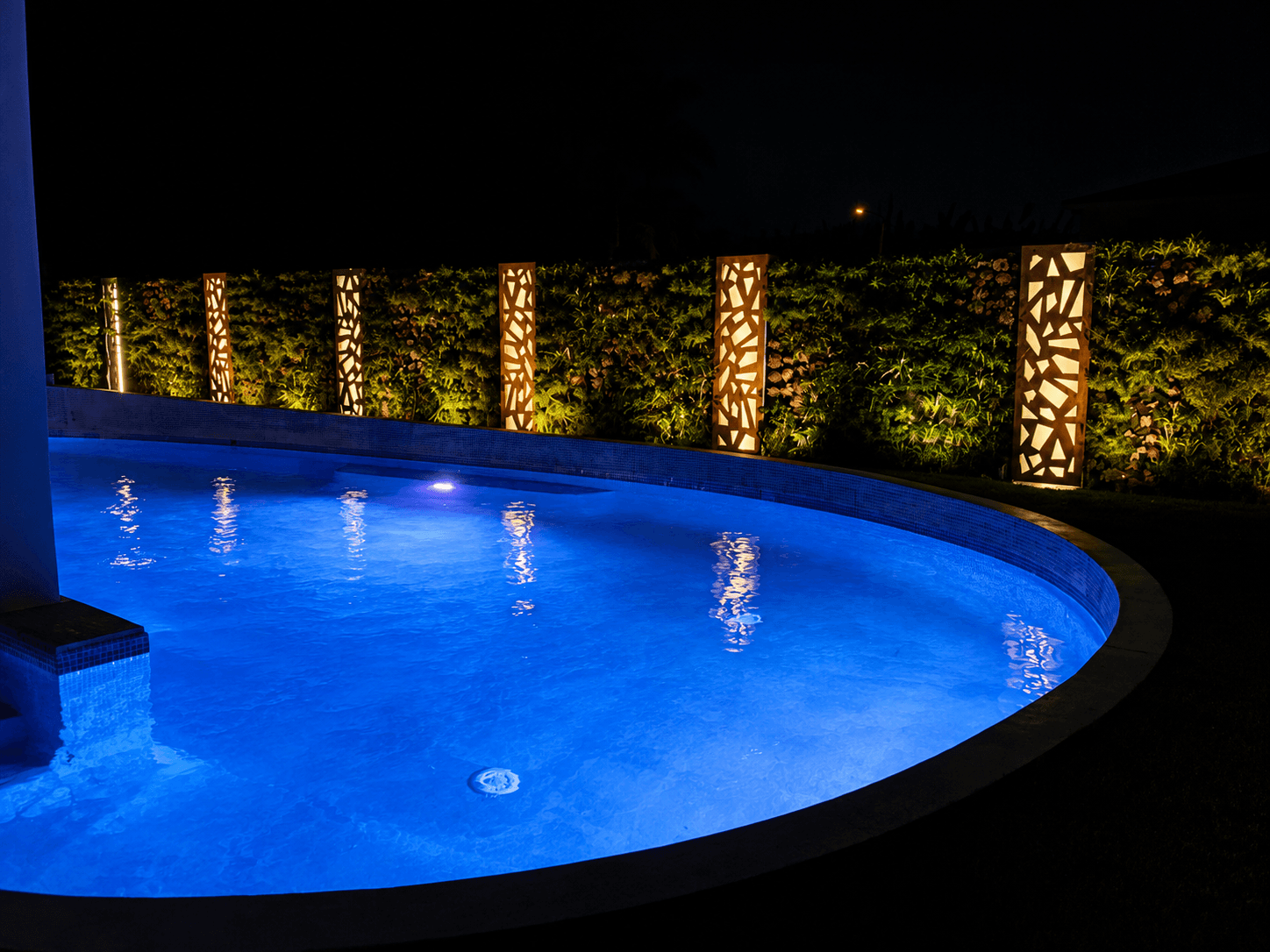 Backlit waterjet light towers by illuminated pool at night