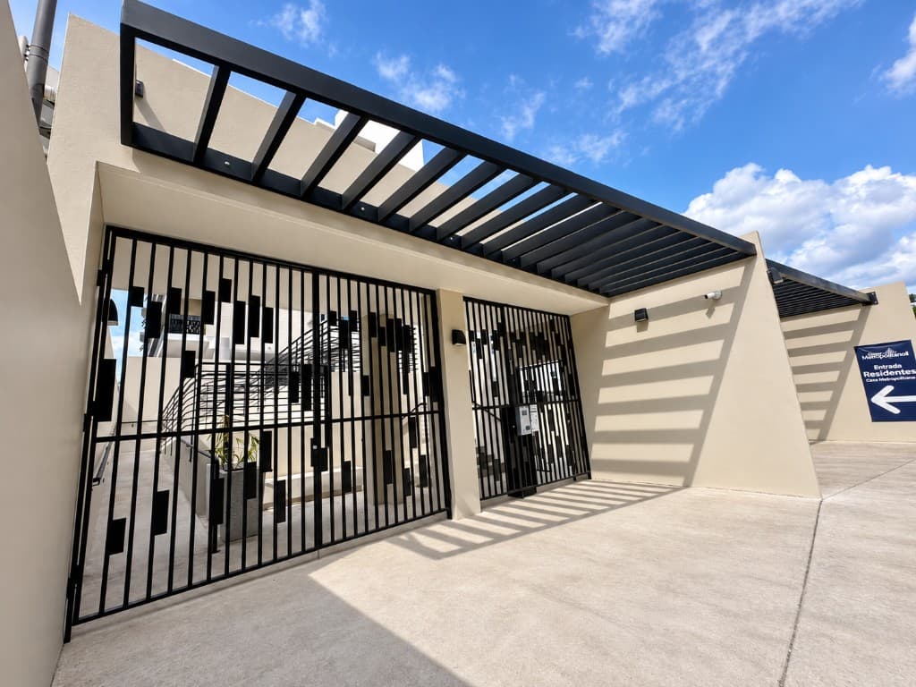 Casa Metropolitana resident entrance with waterjet-cut block-pattern gates and louvered pergola
